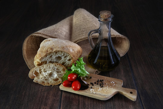 Italian ciabatta bread with bottle of balsamic vinegard and cutting board decorated with pepper, cheese, cherry tomatoes and salad