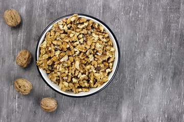 Walnut kernels in a bowl and whole nuts on an old gray table