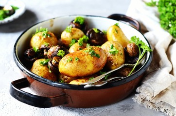 Baked young potatoes with mushrooms in a bowl on a gray background