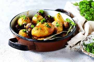 Baked young potatoes with mushrooms in a bowl on a gray background