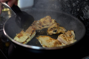 hand cooking chicken meat in a frying pan