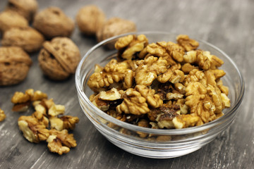 Walnut kernels in a bowl and whole nuts on an old gray table