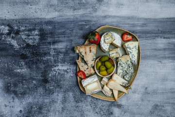 variety of cheese with fresh strawberries, grape, olives and nuts, martini glasses on shabby blue background, top view, party appetizer concept