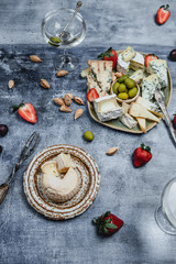 variety of cheese with fresh strawberries, grape, olives and nuts, martini glasses on shabby blue background, top view, party appetizer concept