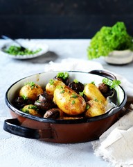 Baked young potatoes with mushrooms in a bowl on a gray background