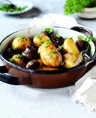 Baked young potatoes with mushrooms in a bowl on a gray background