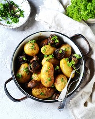 Baked young potatoes with mushrooms in a bowl on a gray background