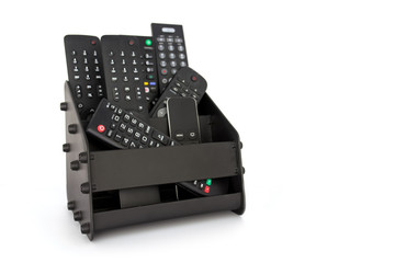 Seven remote controls stacked in black holder on white background.