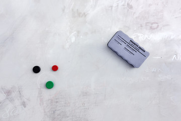 Magnetic eraser sponge and magnets hanging on dirty white board. Text on sponge is translated...