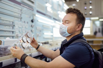 Middle age man wearing protection facemask choosing electric lamps in a hardware store. Countries...