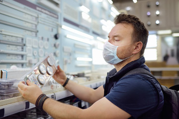 Middle age man wearing protection facemask choosing electric lamps in a hardware store. Countries lifting virus lockdown orders. Social distancing remain.