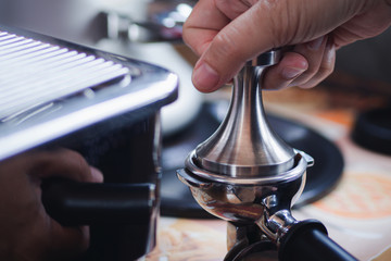 Close-up view of on hands barista presses ground coffee using tamper.