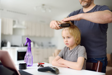 Obraz na płótnie Canvas Preschooler boy gets haircut at home during quarantine. Child watch cartoon movie from tablet pc. Hair cutting for kids by parents while hairdressers closed.