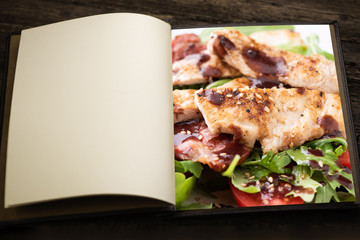 A vintage menu book and image as insert. A chicken salad with rucola bacon and tomato