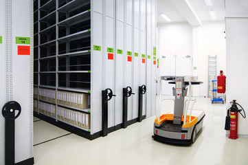 Parked electric lifter in warehouse near to racks for paper document archiving.