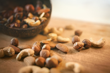 Nuts spilled from coconut bowl on wooden cutting board.