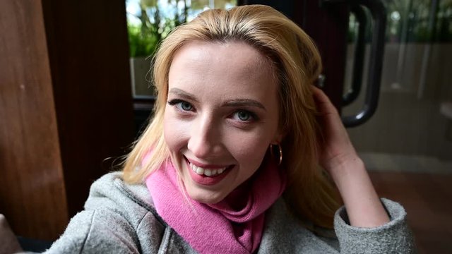 Video of a young caucasian pretty woman taking a selfie with a smile outdoors. Model is wearing a coat in spring.