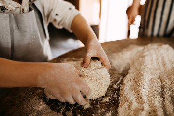 Child making dough for bread, mixing flour on a wooden table surface.