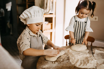 Children making dough for bread, mixing flour on a wooden table surface. Cooking class for children.