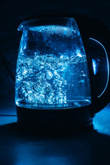 Boiling glass black teapot with blue backlight on a black background. Boiling water. Hot water is...