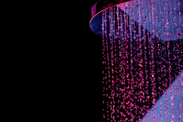 Drops of water fall from a watering can in the shower in red-blue light. Water drops close-up. Flow...