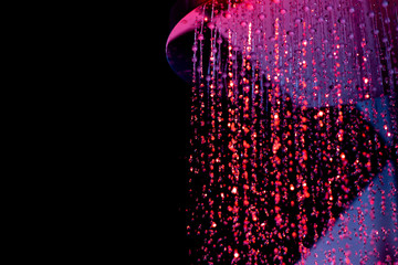 Drops of water fall from a watering can in the shower in red-blue light. Water drops close-up. Flow of water. A large round watering can in the shower..