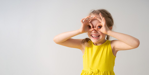 Playful cute little girl looking through her fingers doing goggles, binoculars or mask, smiling...
