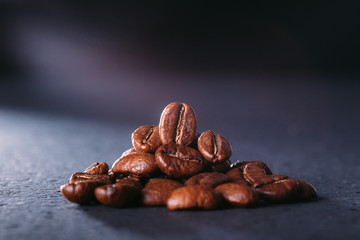 Grains of black coffee on a black granite countertop with yellow light from behind. Advertising photo of coffee. Photo with a glare from the light. Back light on a pyramid with grains..