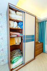 open Built-in wardrobe with bedding. There is a chest of drawers next to it
