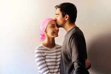 Young woman with a pink scarf next to her husband while he kisses her forehead. Concept of Support...