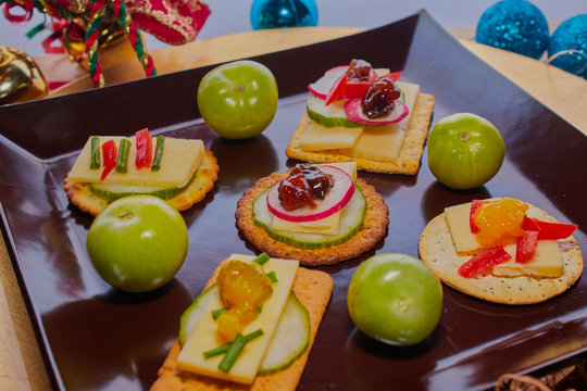 Selection of crackers with various cheeses and vegetables on them there is some Christmas decorations in the background.
