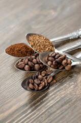 different textures of coffee in spoons on a wooden background, coffee beans, instant coffee, ground coffee