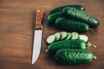 Sliced fresh green cucumbers with a knife on a wooden background. Top view. Copy, empty space for text