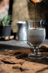 a glass of latte on a table with pieces of dark chocolate and cocoa