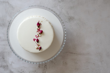 Obraz na płótnie Canvas White mousse cake with smooth glaze decorated with dried rose buds with milk and berry filling, close up. Copy space