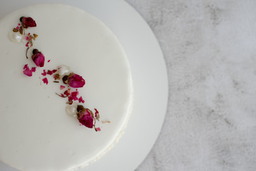 White mousse cake with smooth glaze decorated with dried rose buds  with milk and berry filling, close up. Copy space