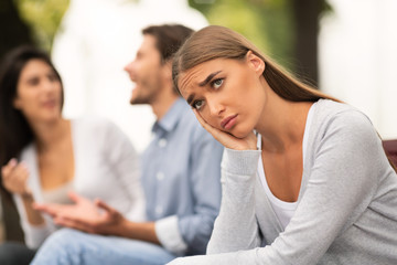 Girl Suffering From Loneliness Sitting Next To Happy Lovers Outdoor