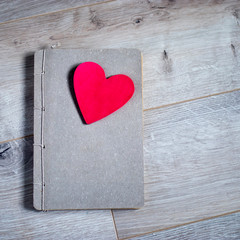 Kraft notebook with red paper heart on a gray wooden table surface. The texture of birch.