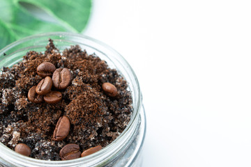 Body scrub from ground coffee and sugar in a glass jar on a background of green leaf monstera. Homemade peeling and spa care product. Close-up.
