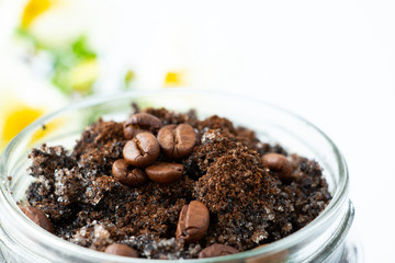 Body scrub from ground coffee and sugar in a glass jar on a blurred floral background. Homemade peeling and spa care product. Close-up.