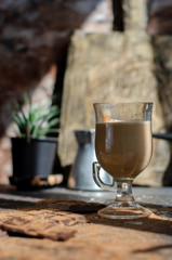 a glass of latte on a table with pieces of dark chocolate and cocoa