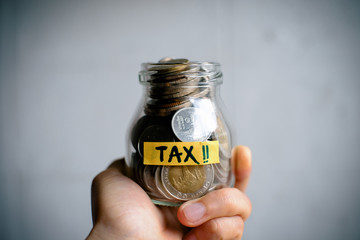 Hand holding money in a jar with TAX word on white background. Financial and tax concept. Thai bath money in a jar. The glass jar full with the coins