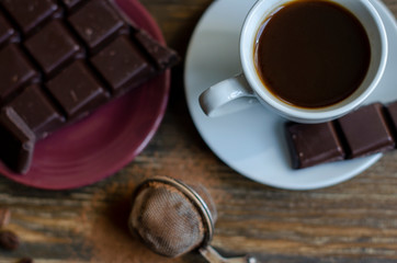 cup of coffee with a piece of chocolate on a wooden background