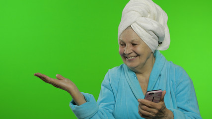 Elderly grandmother in bathrobe. Old woman with smartphone pointing at something