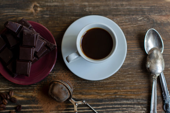 cup of coffee with a piece of chocolate on a wooden background