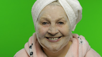 Elderly grandmother after shower. Old woman applying cosmetic bubble face mask