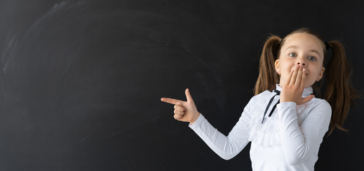 Cheerful schoolgirl in the classroom. A girl stands at the blackboard and laughs. Place for an inscription. Education and development of children of primary school.