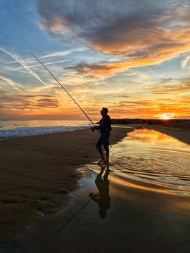 man fishing at sunset on the shore of the beach, surfcasting