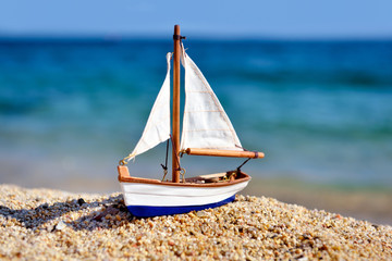 Miniature toy sailboat on the beach against the background of the sea and waves. Vacation and...