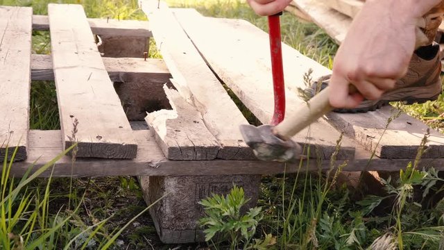 a man disassembles pallets with a crowbar and hammer